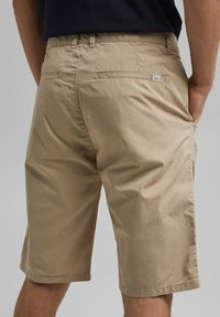 Beżowe szorty z lekkiego materiału, w klasycznym kroju, z bocznymi kieszeniami i dyskretną metką marki z tyłu.