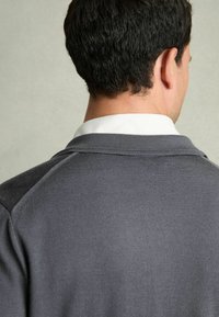 Grå strikket sweater med en tekstureret overflade, der har en hvid krave nedenunder, hvilket viser et afslappet og komfortabelt design.