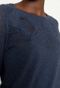 Granatowy sweter z teksturowanymi detalami na ramionach i górnej części klatki piersiowej, wykonany z miękkiego materiału o luźnym kroju.
