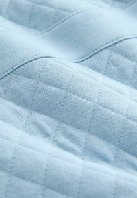 Svetlo modri material s teksturirano, kviltano vzorcem, ki vsebuje dvignjene kvadratke in gladke površine ter prikazuje šive v ukrivljenem dizajnu.