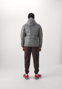 Graue Daunenjacke mit Kapuze, mit gestepptem Design und elastischen Bündchen, kombiniert mit dunklen Hosen und roten Sportschuhen.