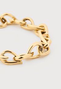 Χοντρό, γυαλιστερό χρυσό βραχιόλι αλυσίδας με μεγάλους, στρογγυλεμένους, αλληλοσυνδεόμενους κρίκους, παρουσιάζεται σε απλό φωτεινό φόντο.