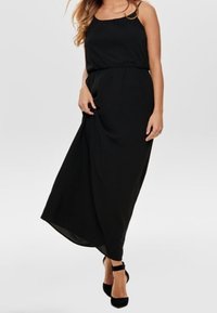 Czarna, bezrękawnikowa sukienka maxi z elastycznym paskiem w talii. Lekka tkanina tworzy gładką sylwetkę. Nosiona z czarnymi szpilkami.