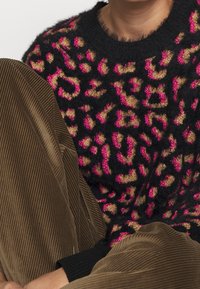 Svart tröja med leopardmönster och rosa samt beige pälsliknande struktur, tillsammans med bruna kordfloddsbyxor med vertikala ränder.