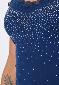 Navyblauw top met een ronde halslijn en kantafwerking, versierd met verspreide heldere rhinestones die een gradiëntpatroon creëren. Zachte stofstructuur.