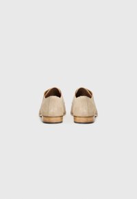 Beige suede shoes with a low heel, round toe, and smooth leather accents. The back features a seamless design and polished wood-like base.