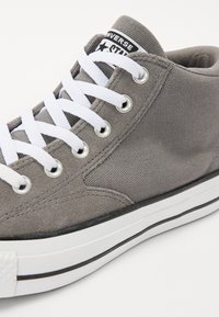 Sneaker alte in tela grigia con lacci bianchi, accenti neri e occhielli metallici. Presenta una finitura testurizzata e una suola in gomma con una striscia nera.