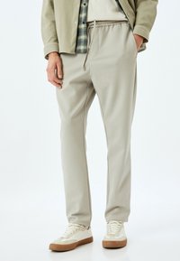 Lysegrå joggerbukser lavet af blødt stof med elastisk talje og snøre, parret med beige sneakers. Glat overflade, lige pasform.