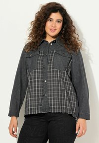 Schwarzes Button-Down-Hemd mit einem Denim-Oberteil und einem karierten unteren Abschnitt in Grautönen; verfügt über zwei Brusttaschen und einen leicht ausgefransten Saum.