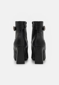 Czarne skórzane botki za kostkę na obcasie blokowym. W skład cech wchodzi pasek z okrągłą klamrą, złożone przeszycia oraz gładka tekstura.