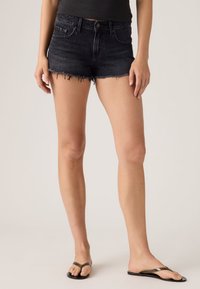 Μαύρα τζιν σορτς με ξεφτισμένο τελείωμα, υψηλή μέση και κλασικό σχέδιο με πέντε τσέπες. Φοριούνται με απλά μαύρα σαγιονάρια.