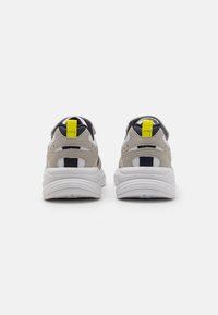 Scarpe sportive beige e blu navy con suola bianca, dotate di un pull tab giallo e realizzate in materiali sintetici e tessili lisci.