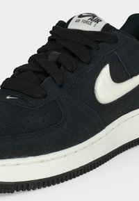 Μαύρο αθλητικό παπούτσι Nike Air Force 1 με λευκό λογότυπο Swoosh, μαύρα κορδόνια και λευκή μεσαία σόλα, σε κοντινή λεπτομέρεια.