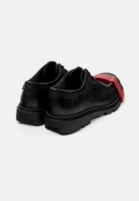 Schwarze Leder Schuhe mit einer schwarzen Gummisohle und roten Kunststoffakzenten an der Zehe. Glatte Textur und abgerundetes Design.