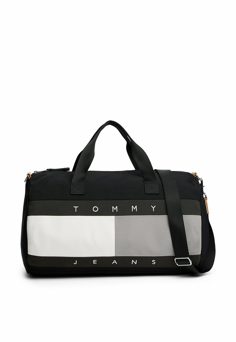 Sort og grå træningstaske med kontrasterende sektioner, iøjnefaldende "TOMMY JEANS" tekst, dobbelt bærehåndtag og en justerbar skulderrem.