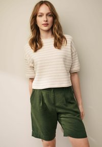 Kortærmet, cremet stribet top med tekstureret stof; parret med grønne linnedshorts med folder og sidelommer.
