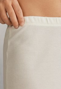 Crème-kleurige, ribbelige stretchstof bij de taille van de shorts, met een zichtbare elastieken band, zachte textuur en vloeiende pasvorm.