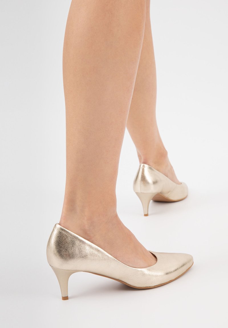 Décolleté metallici oro con punta allungata e tacco a stiletto di 5 cm. Texture liscia con superficie riflettente e design minimalista.