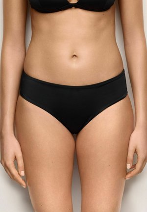 Kobieta nosząca czarne majtki od bikini i pasujący top bikini, pokazująca środkową część ciała i górne partie ud na neutralnym tle.