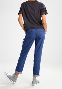 Tmavě šedé tričko s krátkým rukávem a černými pruhy, doplněné modrými džínami s ohrnutými manžetami a světle šedými vysokými teniskami.