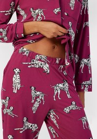 Lilla pyjamasæt med sort-hvide Dalmatiner hundemønstre. Overdelen har lange ærmer og en knap, mens den elastiske talje på bukserne giver komfort.