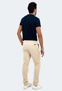 Marinefarbener Rundhalsausschnitt-T-Shirt, kombiniert mit hellbeigen Hosen. Glatter Baumwollstoff, taillierte Form und minimalistisches Design. Weiße Sneakers vervollständigen den Look.