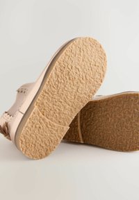 Scarpa in pelle beige con suola in gomma testurizzata, caratterizzata da una forma arrotondata e un design a cinturino. Dettagli notevoli includono accenti a intaglio.
