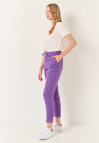 Paarse linnnen joggerbroek met een drawstring taille, zijzakken en een taps toelopend ontwerp. Gecombineerd met een eenvoudig wit T-shirt en witte sneakers.