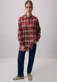 Punane ja kreemikas ruuduline särk nupuga ees, pikkade varrukatega ja lõtva lõikega, kombineeritud tumehallide teksade ja beežide tossudega.