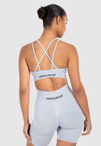 Sujetador deportivo gris claro y pantalones cortos con tejido texturizado. El sujetador cuenta con tirantes cruzados, los pantalones cortos tienen una cinturilla alta con un detalle de logo.