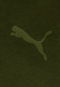 Tessuto a maglia verde oliva con un logo Puma prominente, opaco e di colore verde chiaro, in posizione di salto. Texture con un sottile motivo a coste.
