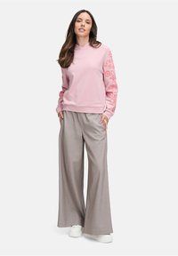 Felpa rosa chiaro con cappuccio e design floreale sulle maniche, abbinata a pantaloni a gamba larga grigi a righe e sneakers bianche.
