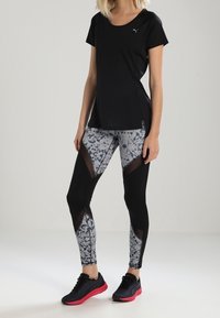 Black short-sleeve athletic top, patterned gray leggings with black accents, and black sneakers with pink soles, featuring mesh inserts.