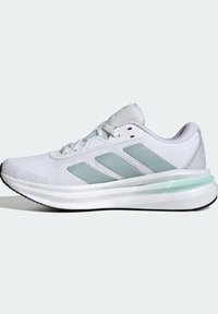 Chaussure de sport blanche avec des rayures vert clair, tige en mesh, semelle intermédiaire amortie et semelle extérieure noire, vue de profil sur un fond uni.