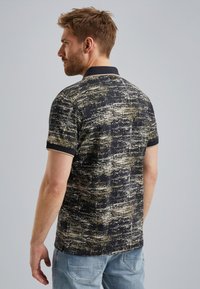 Poloshirt met een gestructureerd zwart en goud patroon. Heeft een donkere kraag en korte mouwen. Gemaakt van ademende stof.