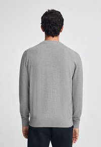 Maglione grigio a maglia con maniche lunghe, scollatura rotonda e orlo a coste. Texture morbida con una finitura liscia, senza motivi o accenti visibili.