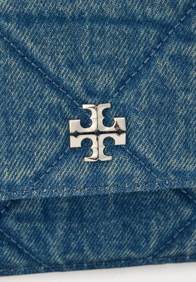Μπλε τζιν ύφασμα με διαγώνια ραφή και ασημί μεταλλικό έμβλημα λογότυπου στο κέντρο του υφάσματος.