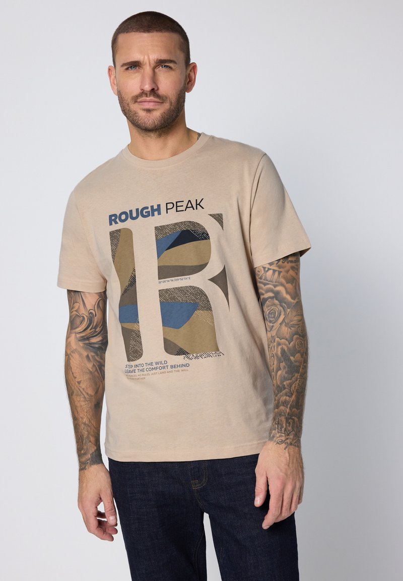 Beige bomulls-t-shirt med tryck som visar blå och bruna former. Texten lyder "ROUGH PEAK" och längst ner finns ett motiverande citat.