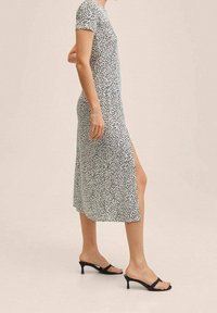 Robe midi à manches courtes blanche à pois noirs, avec une fente latérale. Assortie de sandales à talons noires. Texture de tissu lisse.