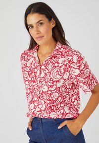Camicetta a maniche corte rossa e bianca con motivo floreale, realizzata in tessuto leggero. Caratterizzata da un colletto, chiusura frontale con bottoni e un motivo floreale vivace.