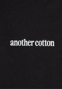 Tessuto di cotone nero con la scritta "another cotton" in carattere serif minuscolo bianco, posizionata centralmente. Texture liscia senza ulteriori motivi.