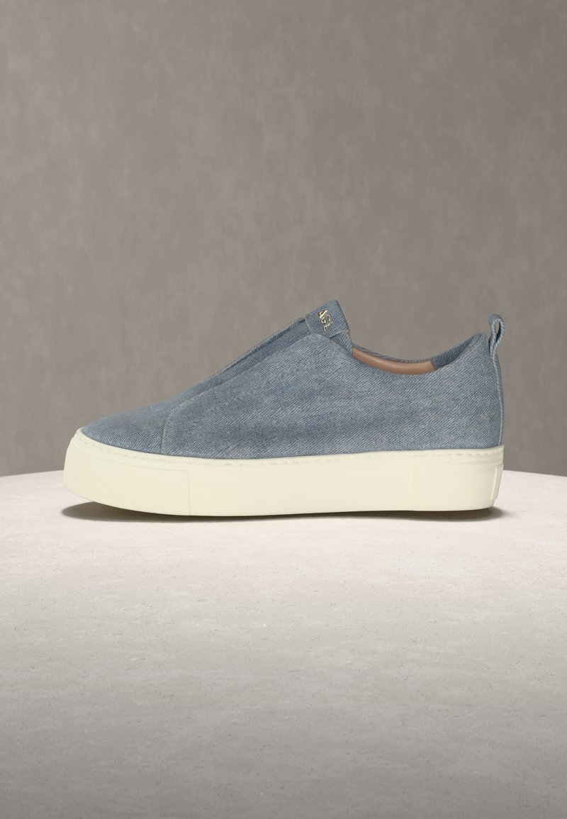 Slip-on αθλητικό παπούτσι με ανώτερο μέρος από τζιν μπλε ύφασμα και παχύ λευκό πέλμα, με μικρή θηλιά τράβηγματος και διακριτικό χρυσό λογότυπο στο πλάι.