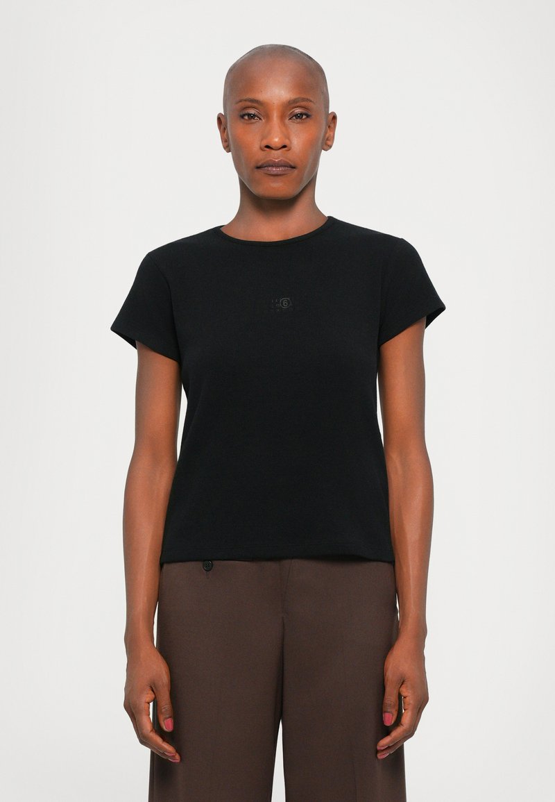 Black cotton T-shirt with short sleeves, round neckline, and subtle logo detail on the chest. Worn with brown trousers.