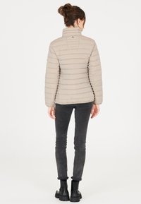 Beige puff jakke med horisontalt quiltet mønster, høj krave og et logodetalje bagpå. Sammen med mørke slim jeans og sorte støvler.