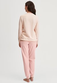 Lichtroze loungewear set bestaande uit een lange mouwen top met textuurstrepen en bijpassende taps toelopende broek. Zachte stof en ribbelmanchetten.