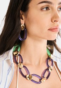 Collar multicolor con grandes eslabones morados y verdes, con acentos dorados. Los pendientes tienen un diseño similar con un acabado dorado.