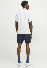 Camisa de manga corta azul claro con cuello, combinada con pantalones cortos azul marino con lunares blancos. Lleva calcetines azules y zapatillas blancas.