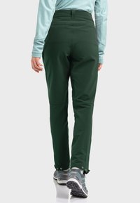 Dark green, water-resistant pants with a high waist, tapered legs, and adjustable cuffs. Paired with gray hiking shoes featuring textured soles.