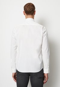 Witte blouse met lange mouwen en een standaard kraag, knoopmanchetten en een gebogen zoom. Zachte stof met een gladde textuur, minimaal ontwerp.