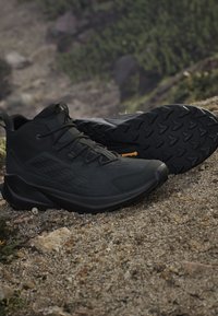 Czarne buty outdoorowe z teksturowaną cholewką, wspierającą konstrukcją i szorstką gumową podeszwą z przyczepnym wzorem. Akcentowane logo.